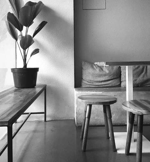 Minimalist cafe seating area with wooden stools, bench, indoor plant, and concrete wall and modern interior design